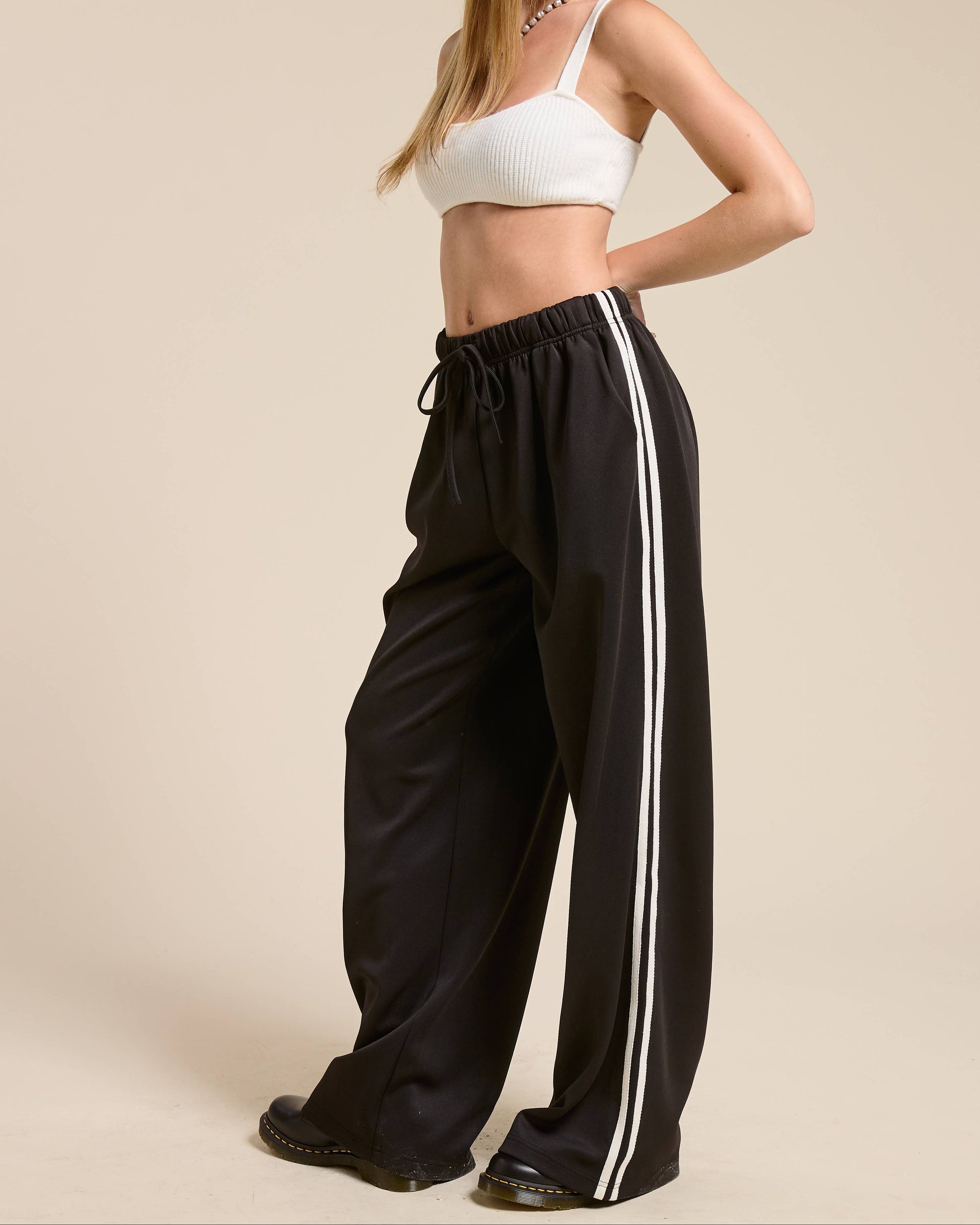 Woman wearing a white crop top and black pants with a white stripe on a beige background